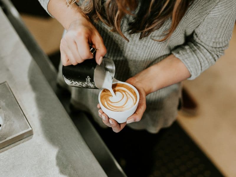 Manos de barista vertiendo leche para dibujar un arte latte en una taza blanca