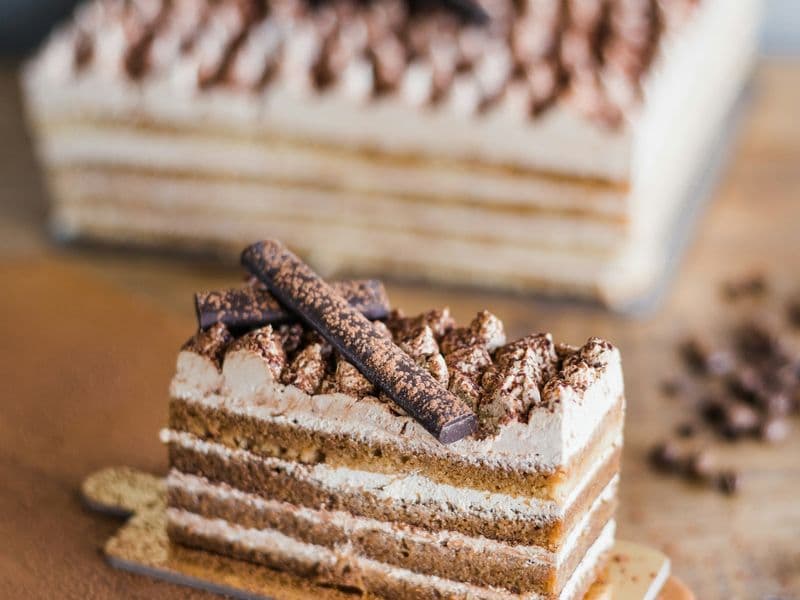 Porción de torta de capas con crema y cacao espolvoreado sobre tabla de madera
